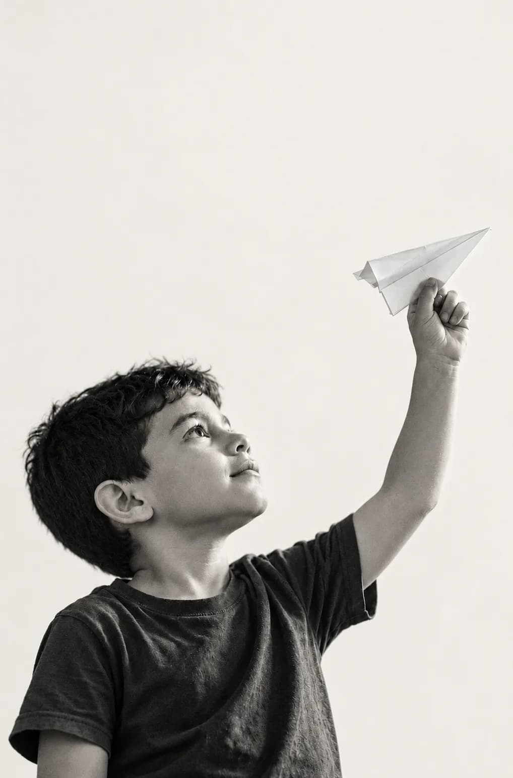 Um menino segura um aviãozinho de papel no alto e olha para ele.